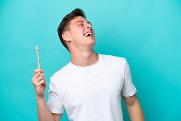 Young Brazilian man brushing teeth isolated on blue background laughing