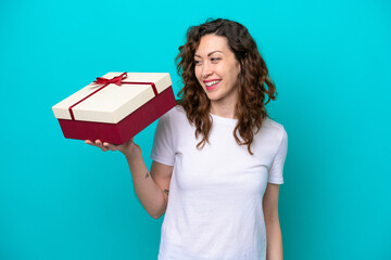 Young caucasian woman holding a gift isolated on blue background with happy expression