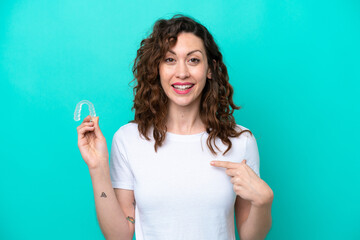 Young caucasian woman holding a envisaging isolated on blue background with surprise facial expression - obrazy, fototapety, plakaty
