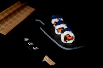 Dish on black background.
View of portion of Japanese sushi roll with caviar, mango, salmon and gourd. 