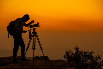 Man photographer on the cliff of the mountain on sunset background