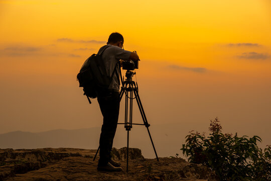 Man photographer on the cliff of the mountain on sunset background