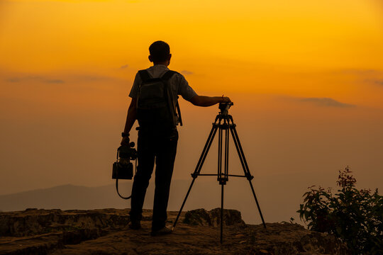 Man photographer on the cliff of the mountain on sunset background