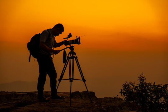 Man photographer on the cliff of the mountain on sunset background