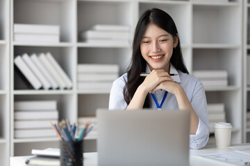 Attractive Asian businesswoman working with laptop and paperwork on office desk.