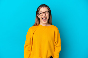 Young caucasian woman isolated on blue background shouting to the front with mouth wide open