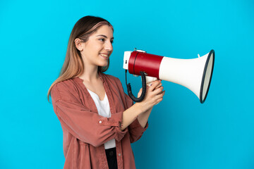Young caucasian woman isolated on blue background shouting through a megaphone to announce something
