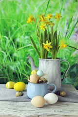 Easter eggs and a bouquet of daffodils in a jug, on a wooden table, against a background of a green lawn, Easter still life