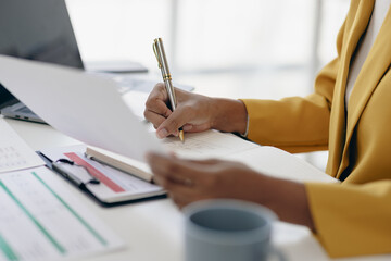 African businesswoman doing paperwork, writing notes and analyzing financial data.