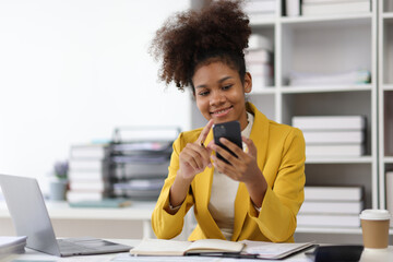 Attractive african american businesswoman using smartphone and doing paperwork in office....