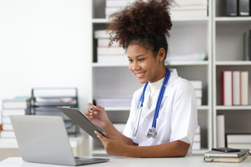 African female doctor in office doing paperwork and writing prescriptions.