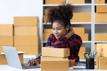 Young African woman starting an online shopping business from home is preparing packages to deliver...