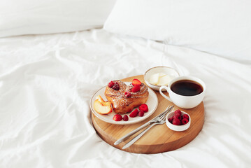 Wooden tray with romantic breakfast for Valentine's Day on white soft bed