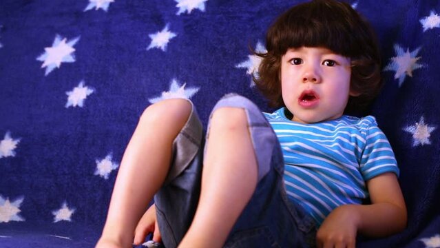 Little boy lies on sofa covered with blue coverlet.