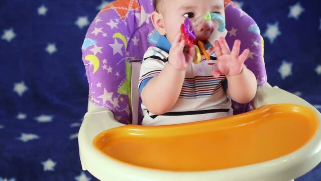 Baby boy sits on highchair and nibbles teething ring.
