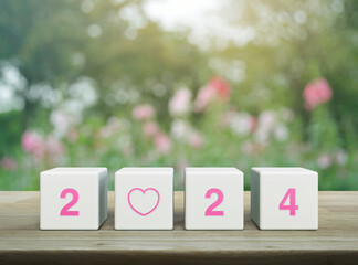 Love icon with 2024 letter on white block cubes on wooden table over blur pink flower and tree in garden, Happy new year 2024 and Valentines day concept