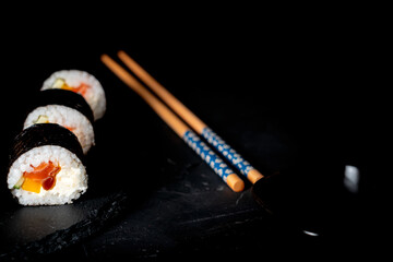 Sushi roll with salmon, mango, calabash and spyta souce  Sushi chopsticks on a black background
Sushi on black background with chopsticks.