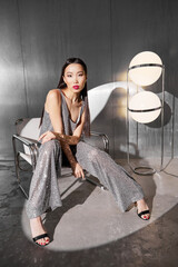 Fashion asian female model in metallic silver glitter suit posing on metallic modern futuristic location.