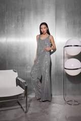 Fashion asian female model in metallic silver glitter suit posing on metallic modern futuristic location.