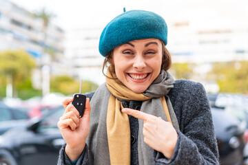 Brunette woman holding car keys at outdoors with surprise facial expression