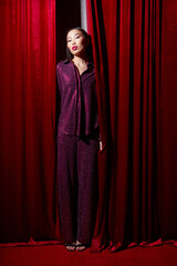 Fashion asian female model in burgundy glitter suit, on red fabric background.
