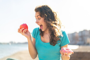 Young sport woman at outdoors holding apple and donut with happy expression