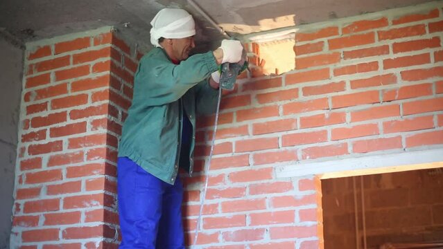 Worker in workwear makes hole in wall with large perforator
