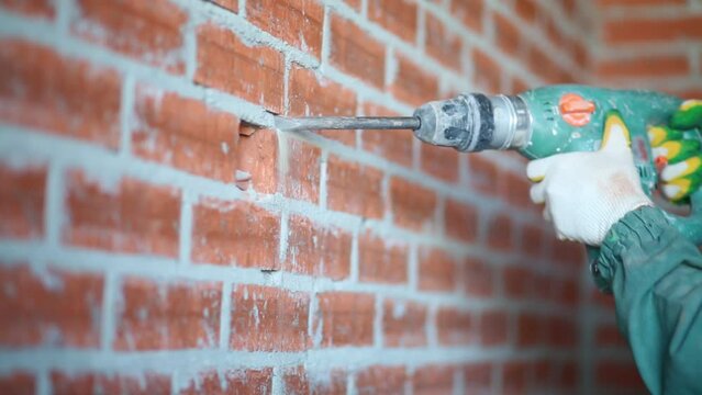 Male hands holding perforator breaking red brick wall