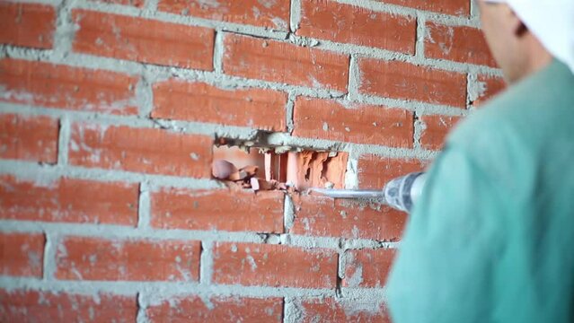 Hands on man in holding perforator making hole in brick wall