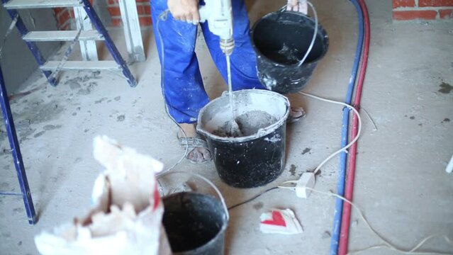 Legs of worker with hand mixer preparing mix for plaster wall