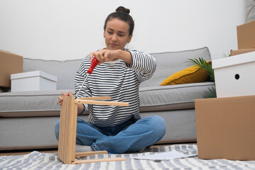 Attractive woman with instrument assembling furniture after shopping at hardware store sitting on...