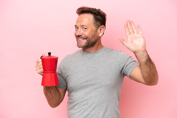 Middle age caucasian man holding coffee pot isolated on pink background saluting with hand with...