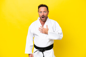 Middle age caucasian man doing karate isolated on yellow background surprised and shocked while looking right