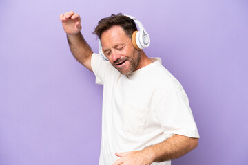 Middle age caucasian man isolated on purple background listening music and dancing