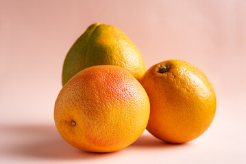 Three grapefruits in various stages of ripeness on a pink background, close-up.