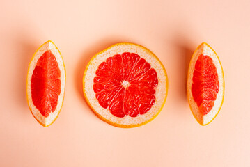 Slice of grapefruit in the middle of two pieces of the same fruit on a pink background,top view.