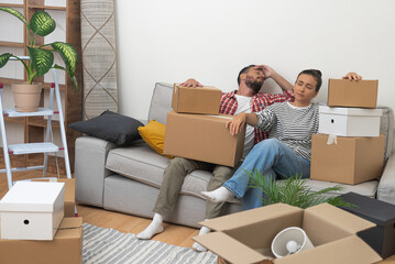 Tired man and woman relaxing on sofa after carrying packed boxes with decorative elements for new...