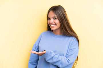 Obraz premium Young caucasian woman isolated on yellow background presenting an idea while looking smiling towards