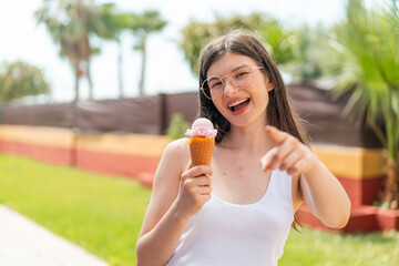 Young pretty Ukrainian woman with a cornet ice cream at outdoors points finger at you with a confident expression