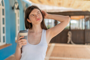 Young pretty Ukrainian woman holding a take away coffee at outdoors having doubts and with confuse face expression