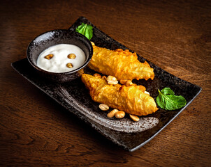 Asian cuisine. Battered bananas and coconut milk sauce in black ceramic dishes
