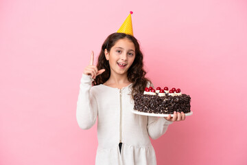 Little caucasian girl holding birthday cake isolated on pink background pointing up a great idea