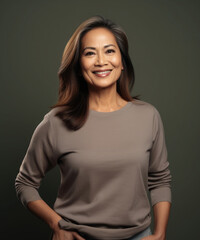 Studio portrait of an elegant and confident filipino woman in her 60s smiling and standing against a grey background 