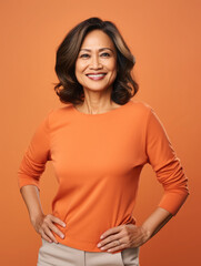 Middle-aged filipino woman smiling and posing confidently on a orange background. Businesswoman studio portrait 
