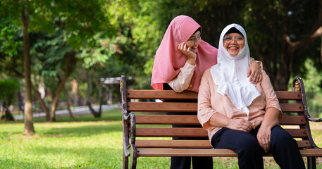 Fototapeta premium Muslim careful caregiver or nurse taking care of the patient in the hospital park. Happy Muslim mother in hijab hugging daughter. Concept of Savings and Senior Health Insurance, a Happy Family