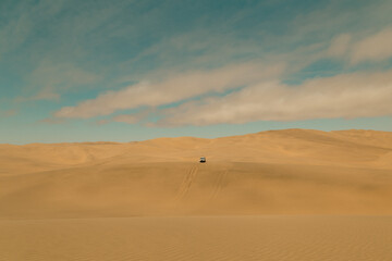 Fototapeta na wymiar Car driving the sand dunes in Sandwich Harbour Historic, Namibia