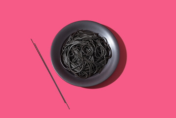 Espaguetis de tinta de calamar negro en un plato sobre fondo rosa. Vista superior	