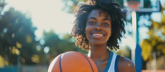 Cool African American girl having fun outdoors, playing basketball at a stylish court.