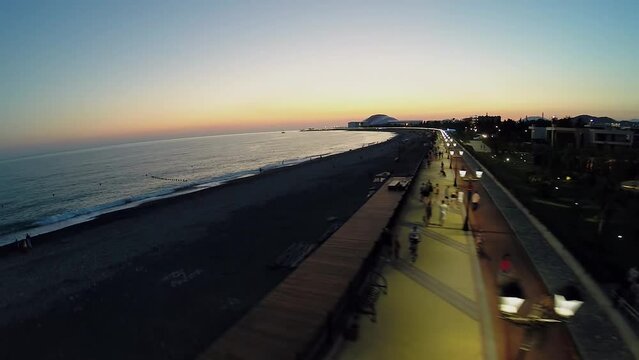 Tourists walk by quay on sea shore at summer evening. Aerial view