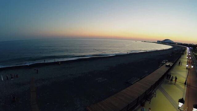 People walk by quay near sea beach at summer evening. Aerial view